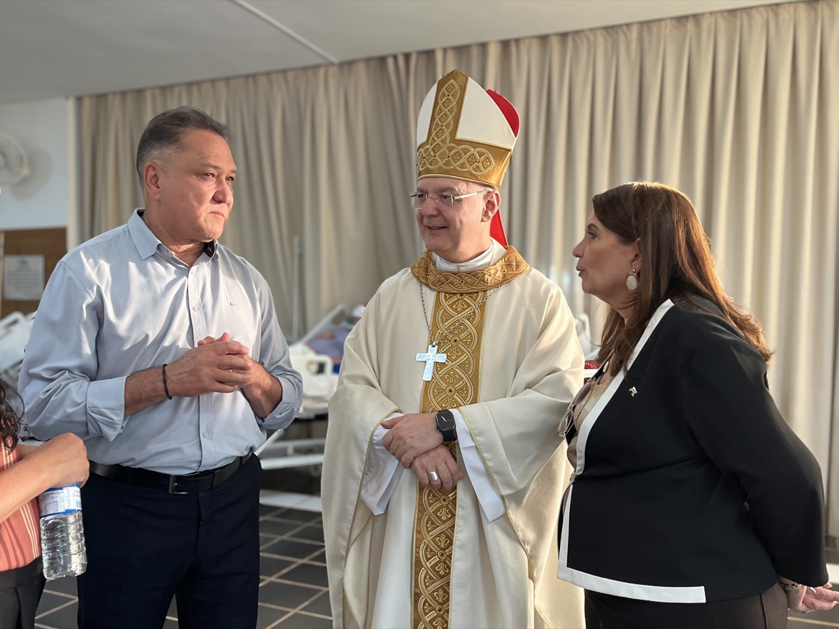 João Cardoso e Bia Kicis conversando com um bispo em ambiente hospitalar, com leitos ao fundo